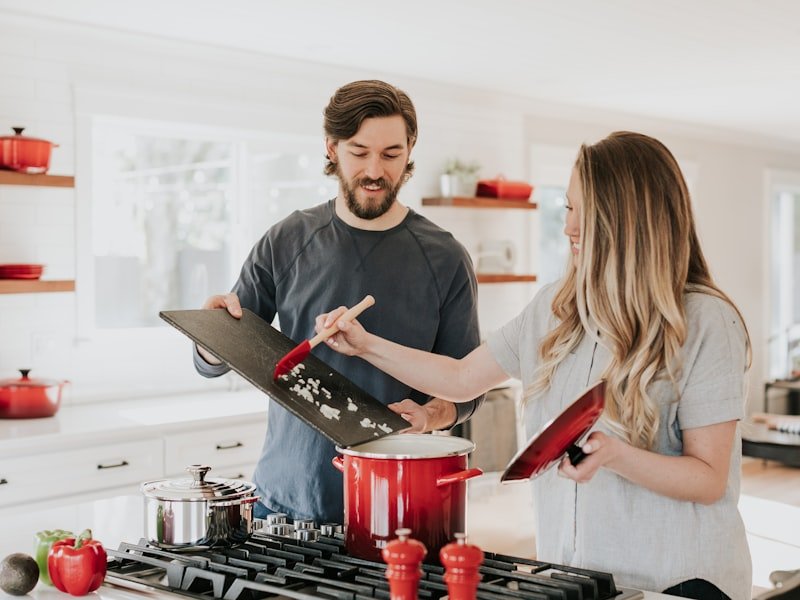 Couple cooking together at a bright white kitchen counter with red pots